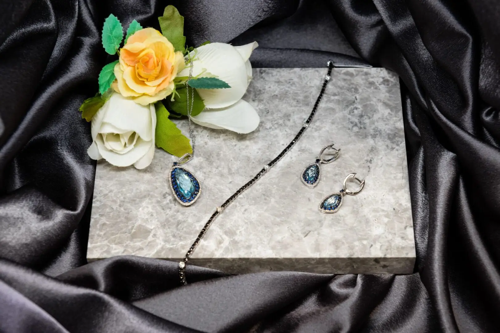 A marble board with two earrings and a flower on it.
